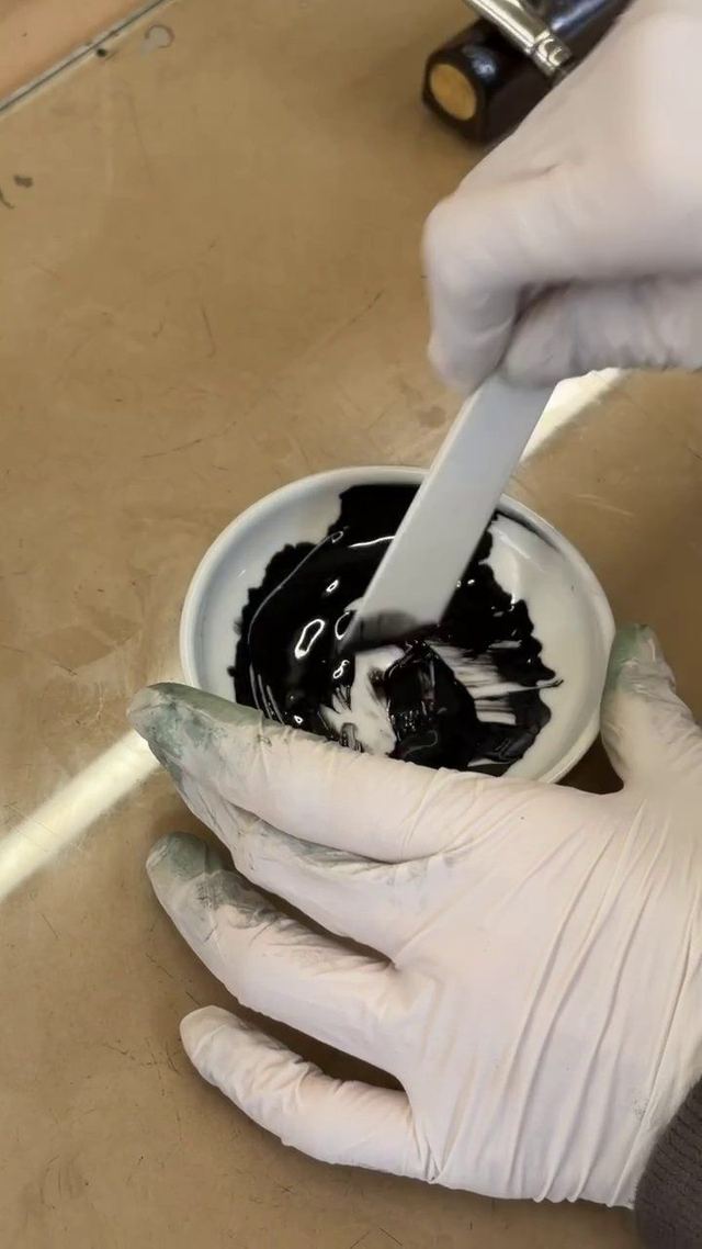 Gloved hands folding glossy black urushi in a small dish