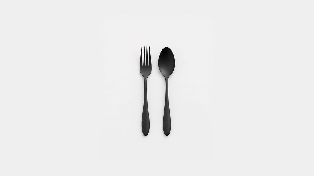 A black urushi-finished stainless steel fork and teardrop-shaped spoon side by side on a light background