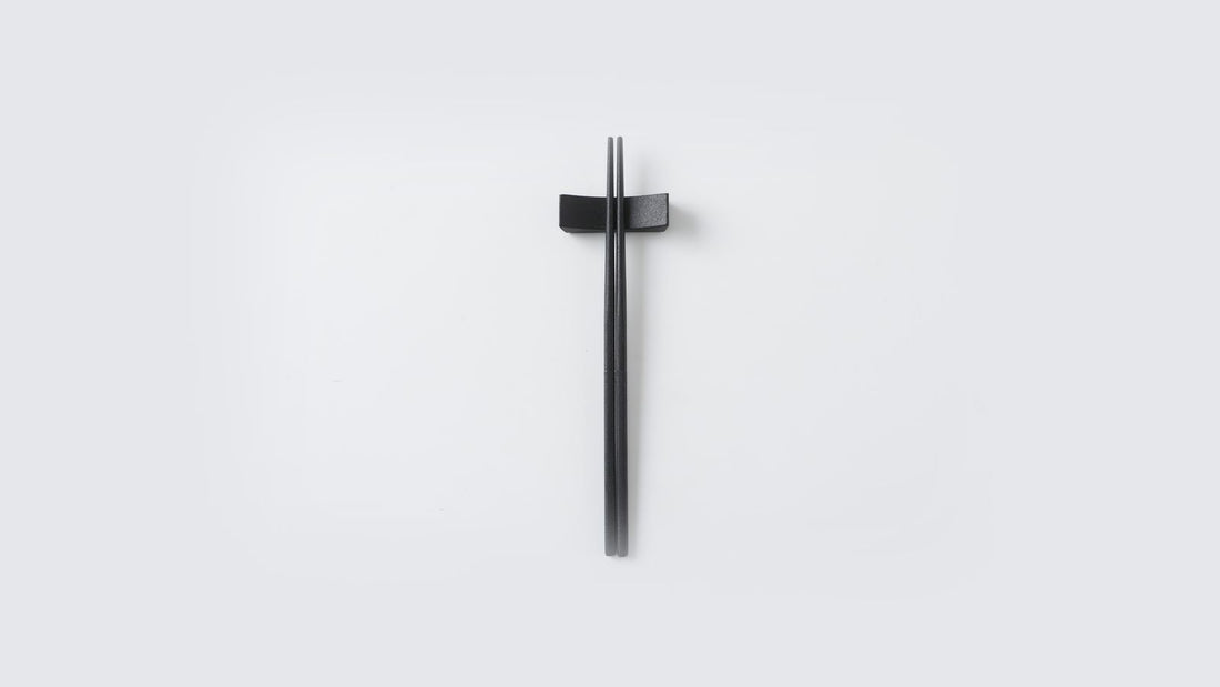 Black urushi-finished stainless steel chopsticks on a matching rest