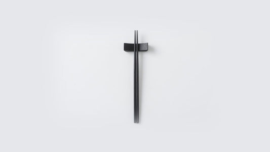 Black urushi-finished stainless steel chopsticks on a matching rest