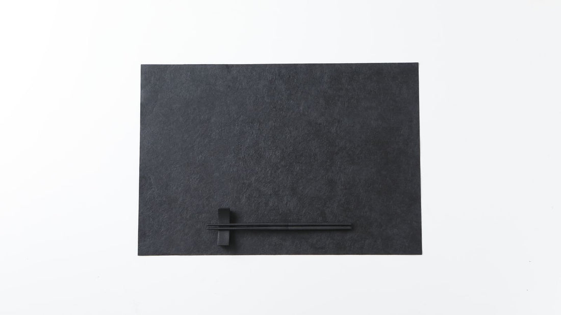 Black urushi-finished Mino washi placemat with chopsticks on a rest, on a white background