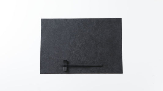 Black urushi-finished Mino washi placemat with chopsticks on a rest, on a white background