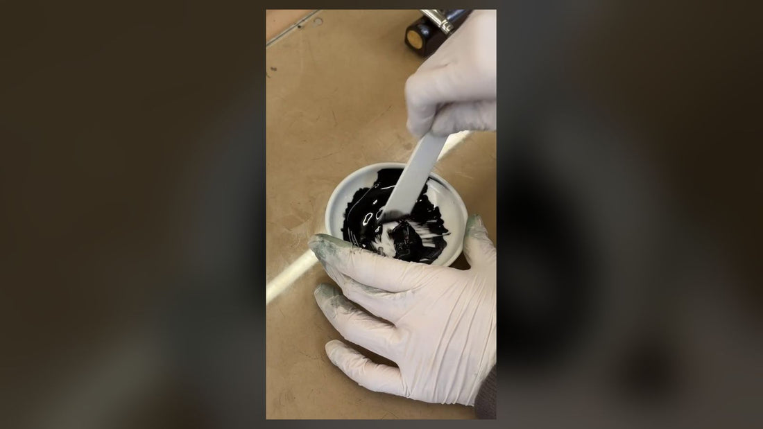 Gloved hands stirring raw urushi lacquer in a small white bowl at a Kyoto workbench