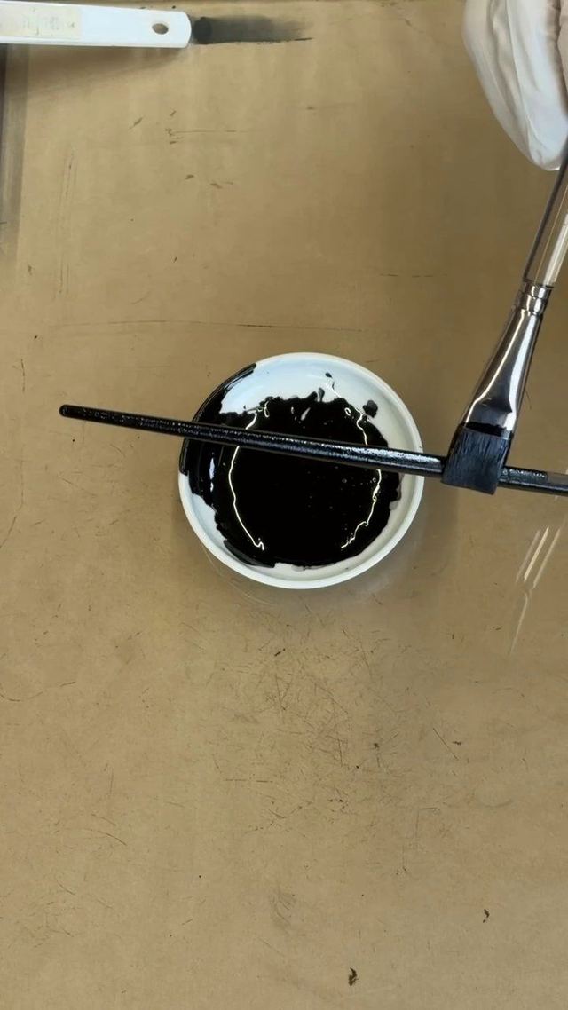 A flat brush laying urushi onto a stainless steel chopstick
