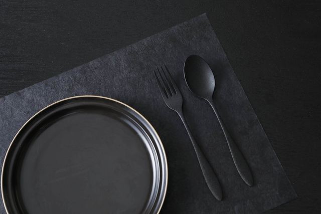 Black urushi spoon and fork on a black washi placemat beside a plate