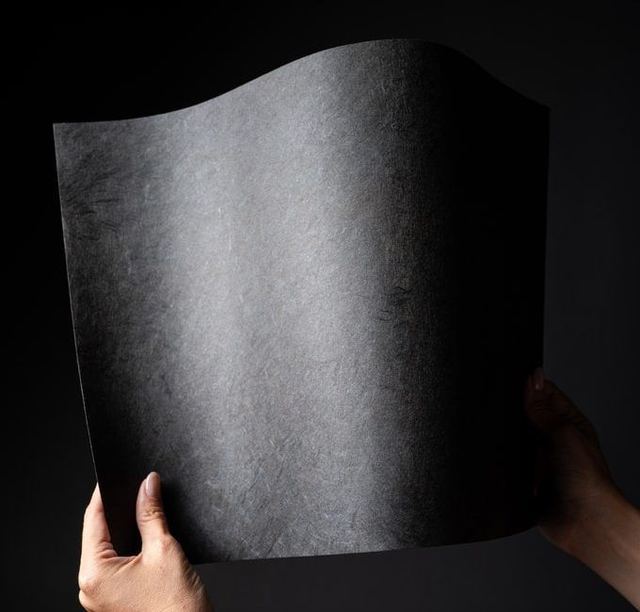 Two hands holding a sheet of black urushi-finished Mino washi